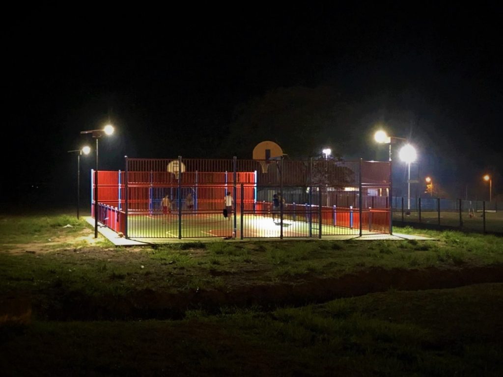 il y a un terrain de sport éclairé avec des lampadaires solaires solamaz avec des enfants qui jouent le soir au football